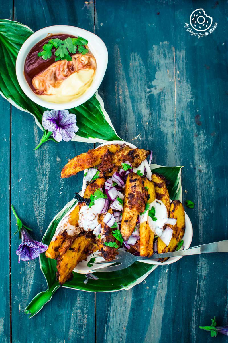 a plate of baked masala potato wedges with a bowl of sauce on the side