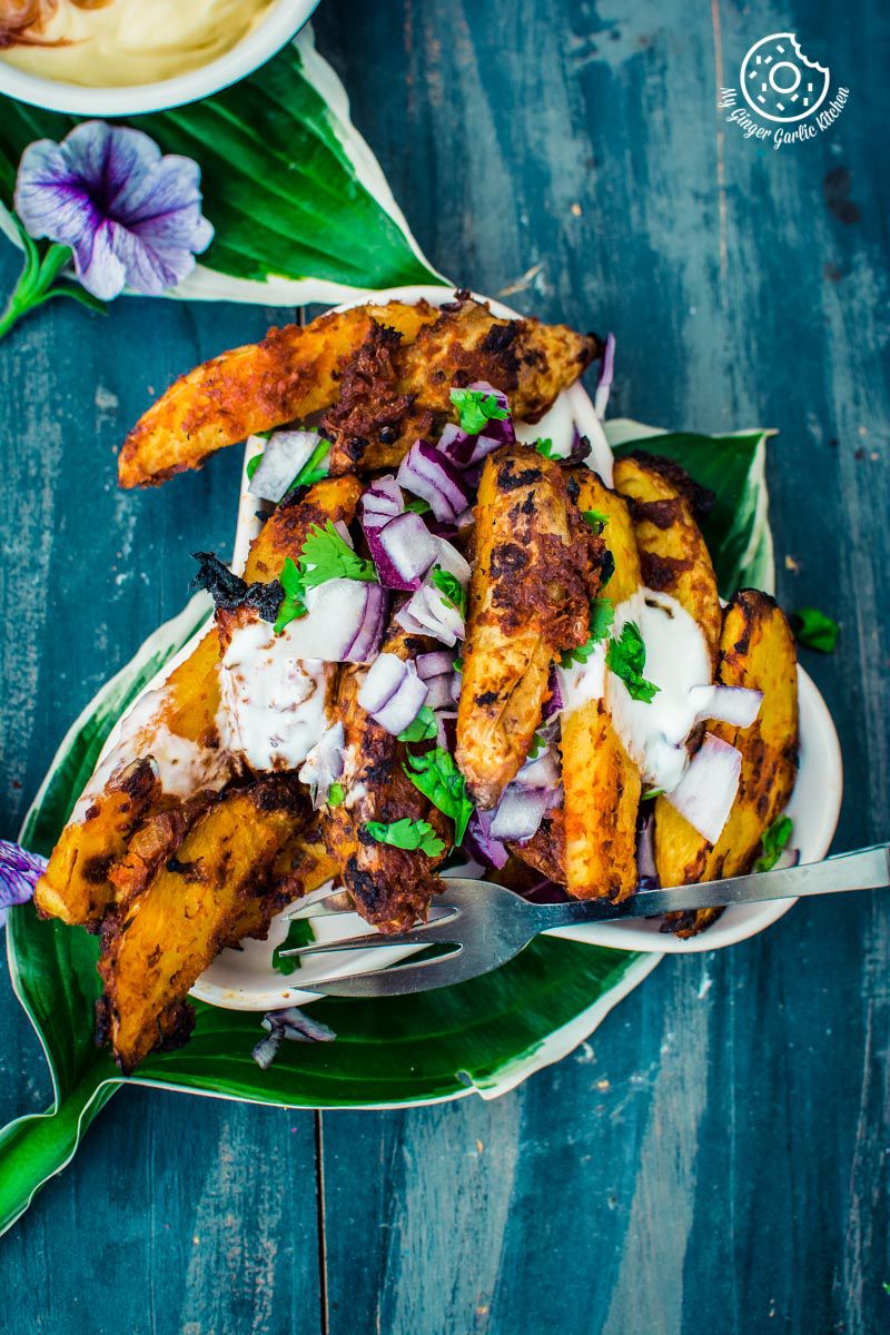 a plate of baked masala potato wedges with some flowers and leaves on a table