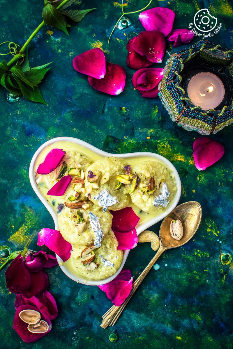 a close up of a plate of soft rasmalai with a spoon and rose petals