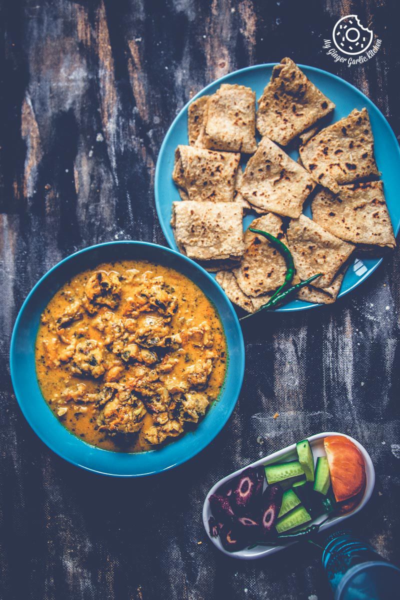 a plate of indian fritters curry garnished with cilantro, and a plate of parathas on a table
