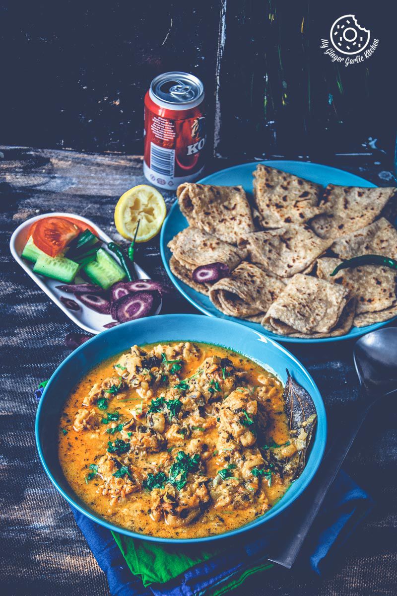 a plate of pakode ki sabji garnished with cilantro with plate of parathas on a table