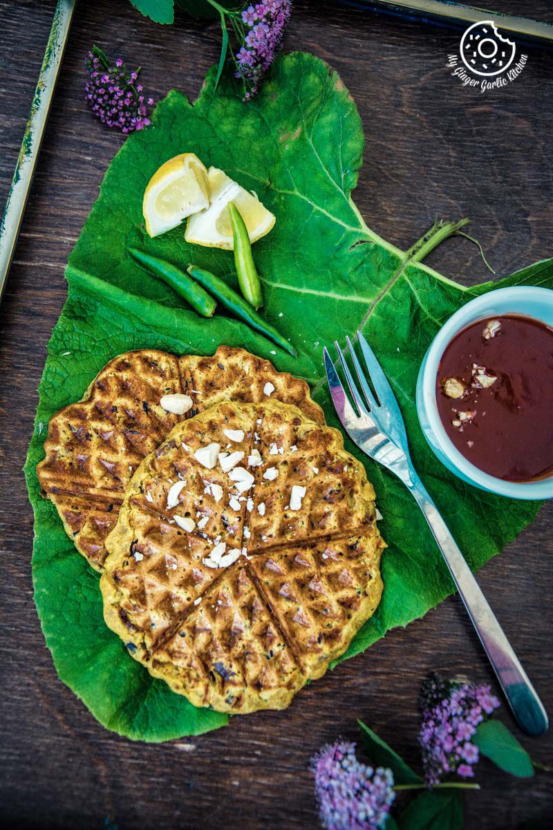 spicy zucchini waffles aka besan chilla waffles on a leaf with a fork and a bowl of sauce