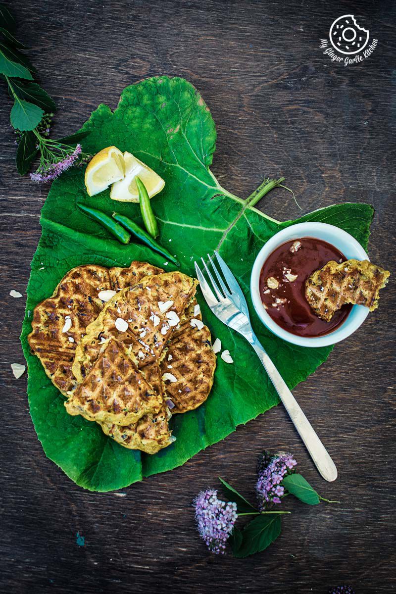 spicy zucchini waffles on a leaf with a fork and a bowl of sauce
