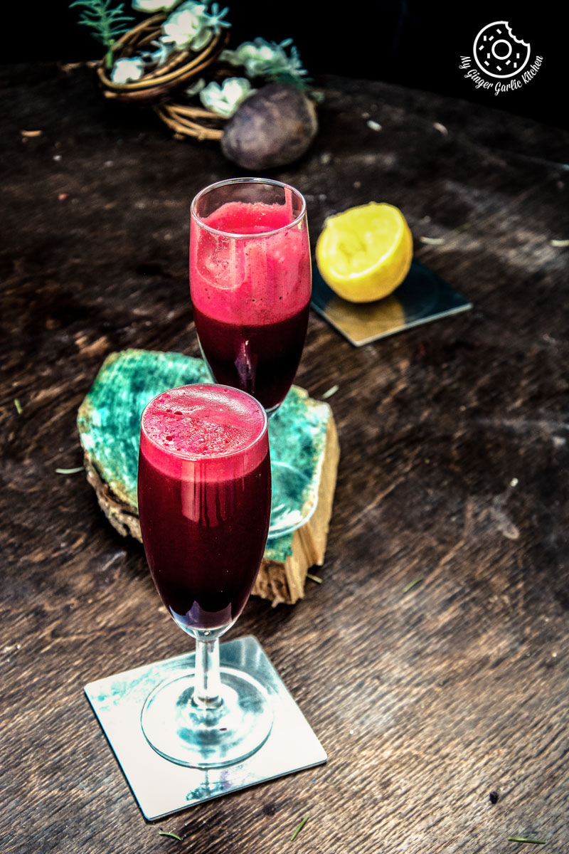 two glasses of detox heart beet juice sitting on a table with a slice of lemon