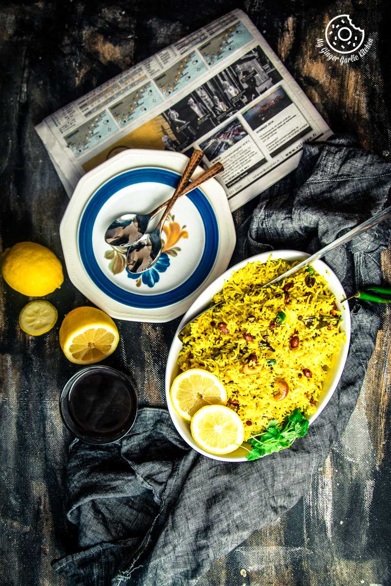 a bowl of south indian lemon rice and a plate with spoons and a news paper on a table