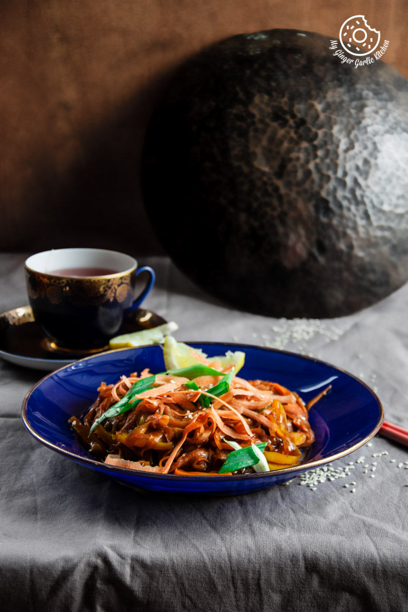 a plate of szechuan spiced carrot fettuccine on a table with a cup of tea
