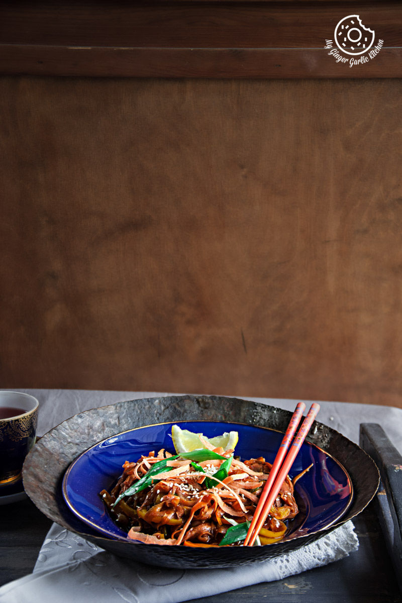 a plate of szechuan spiced carrot fettuccine with chopsticks and a bowl of sauce