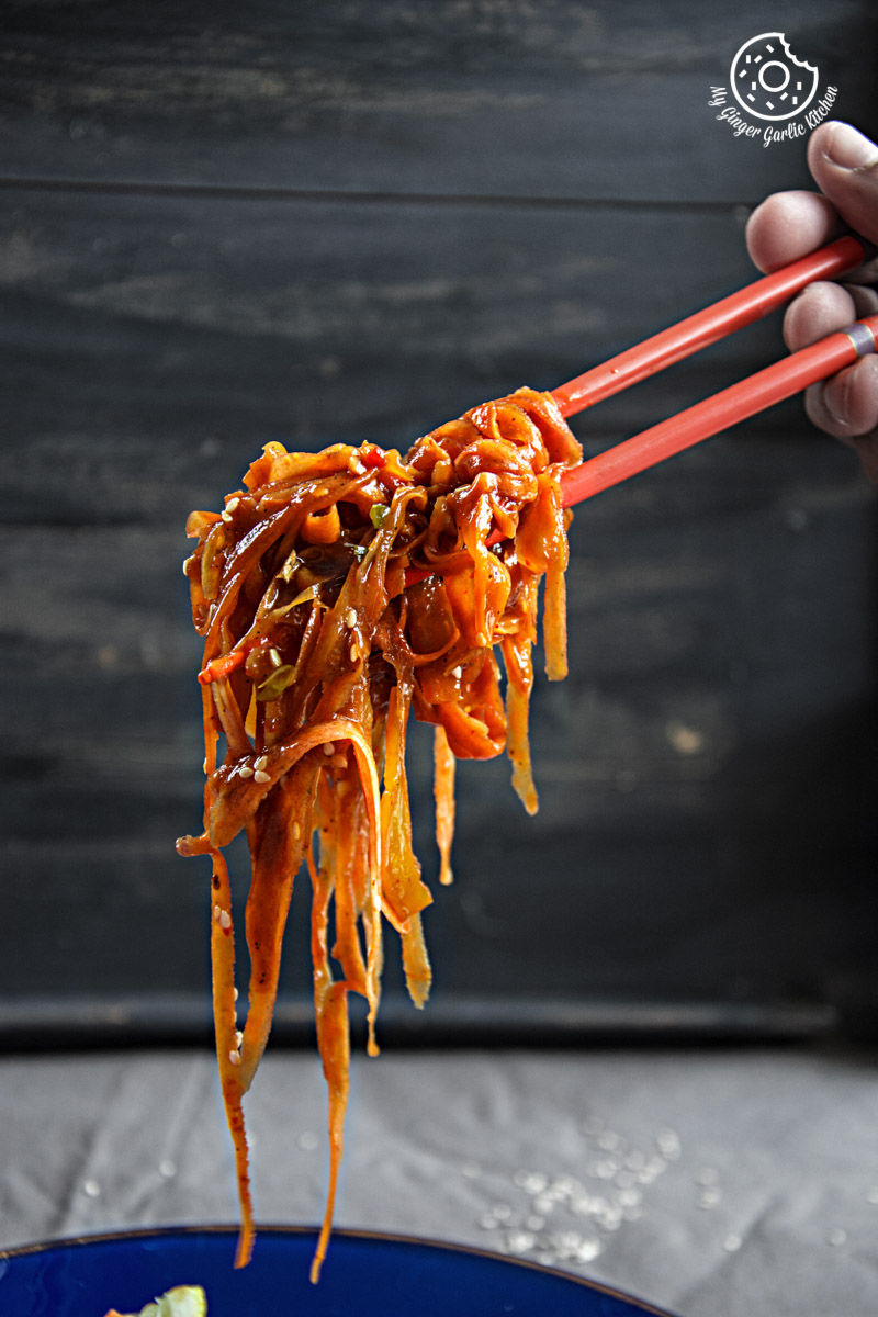 someone holding chopsticks over a plate of szechuan spiced carrot fettuccine