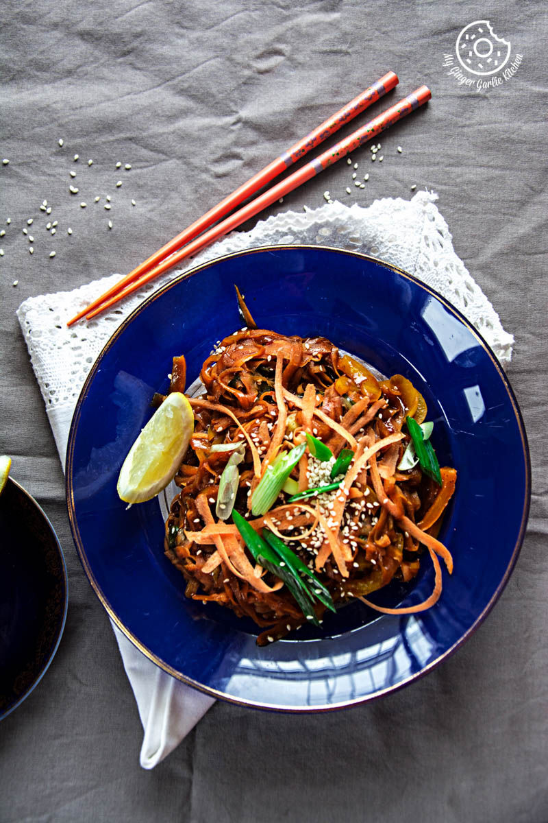 a blue plate with szechuan spiced carrot fettuccine and chopsticks on a table