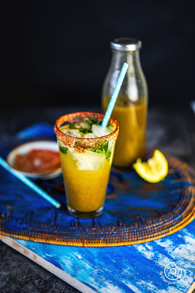 a glass of aam panna with a aam panna bottle in the background