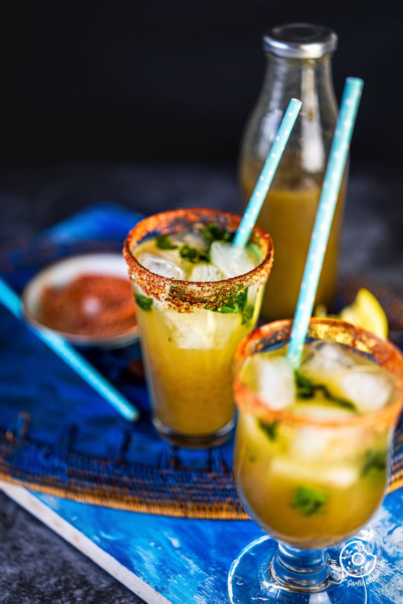 two glasses of aam panna with a aam panna bottle in the background