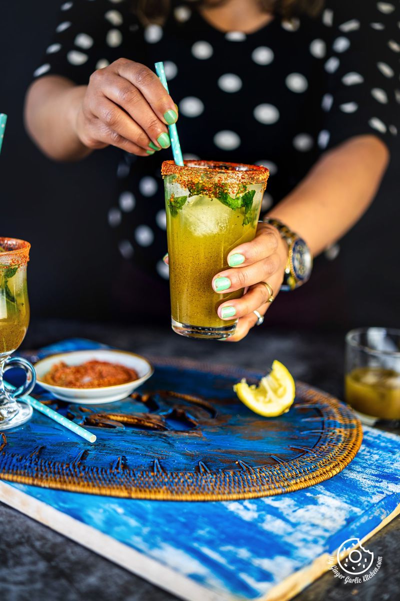 a hand pouring aam panna from a glass bottle in a glass