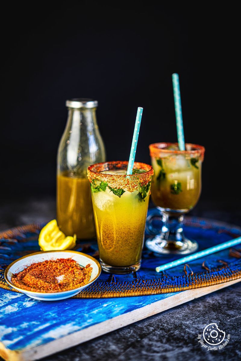 two glasses of aam panna with a aam panna bottle in the background