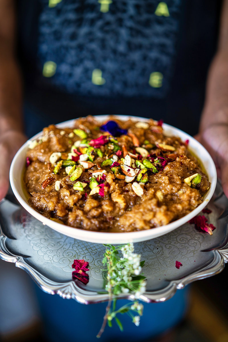 A bowl of Atte Ka Halwa held by a person, beautifully topped with nuts and petals, ready to be served.