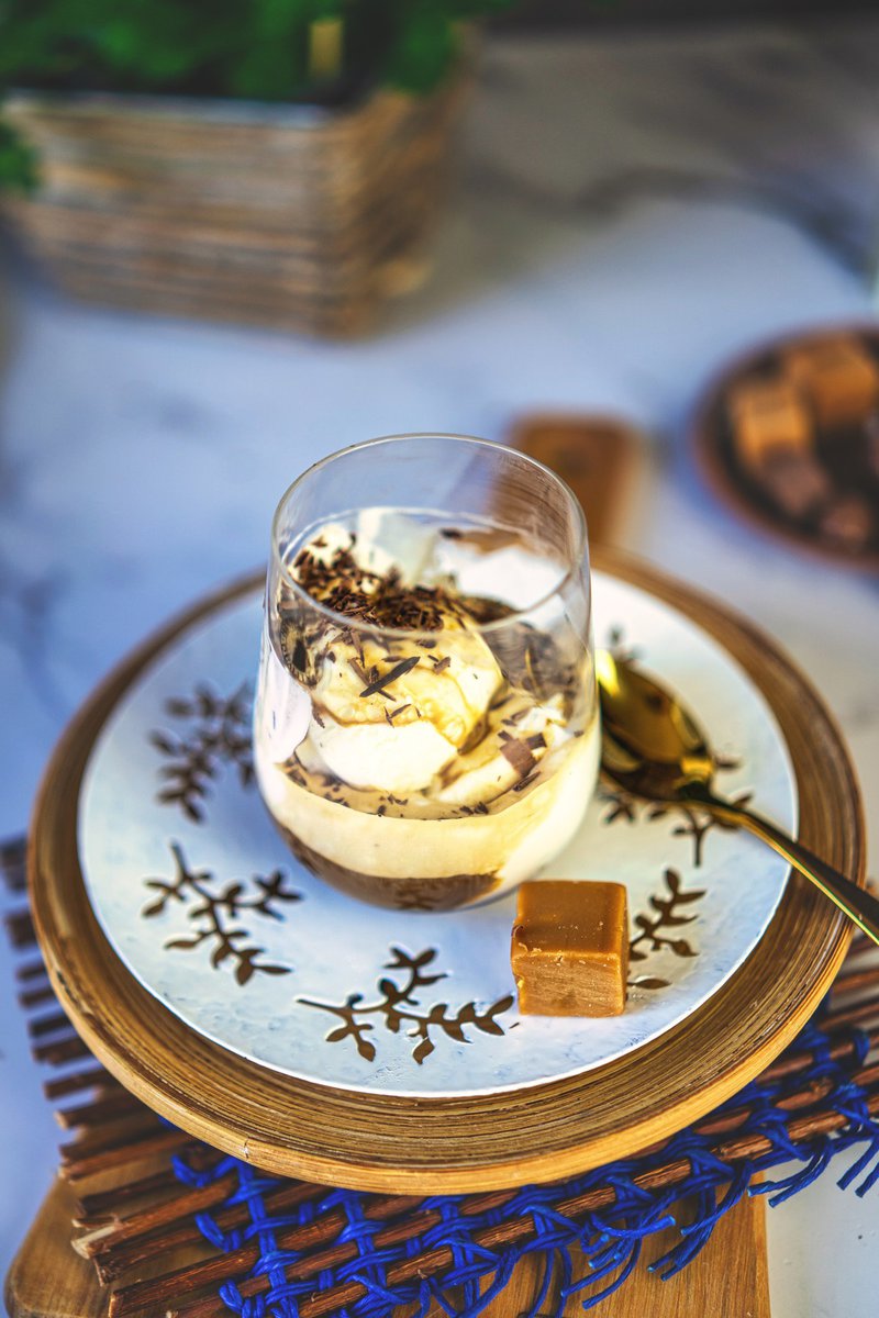  Glass of affogato on a decorative plate with leaf patterns, accompanied by a caramel cube, set on a wooden tray with blue accents.