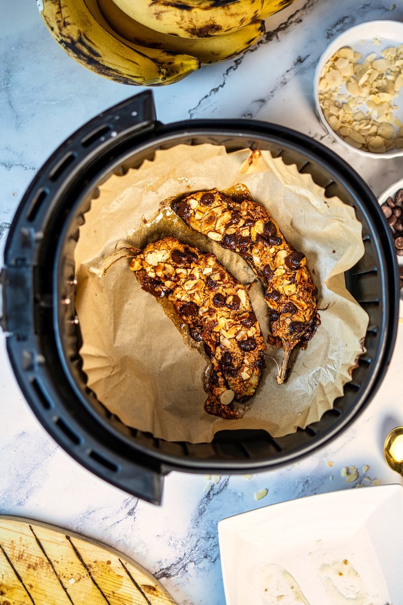 Air Fryer Banana cooking in the air fryer basket with peanut butter, dark chocolate chips, and toasted sliced almonds.