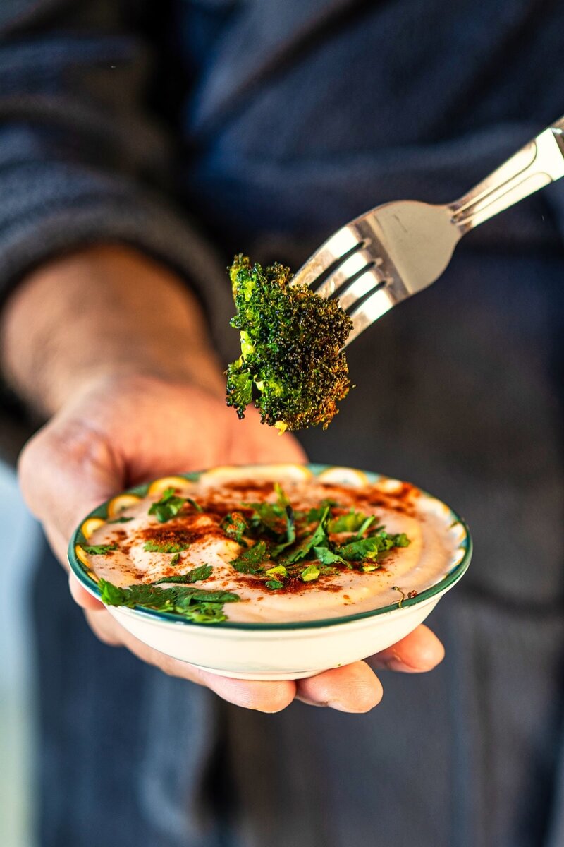 Crispy roasted garlic butter broccoli floret dipped into creamy yogurt sriracha sauce