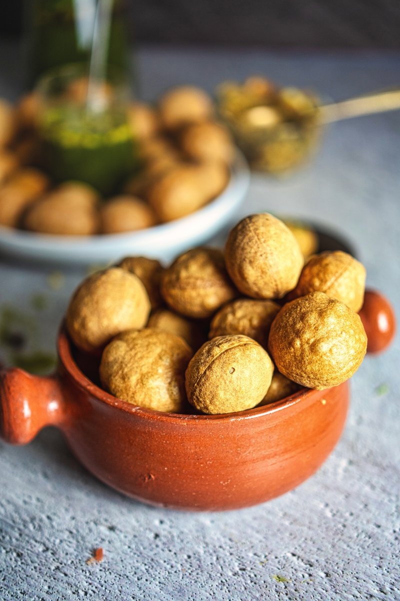 Rustic bowl filled with air-fried puris, with a tray of puris and pani in the background.