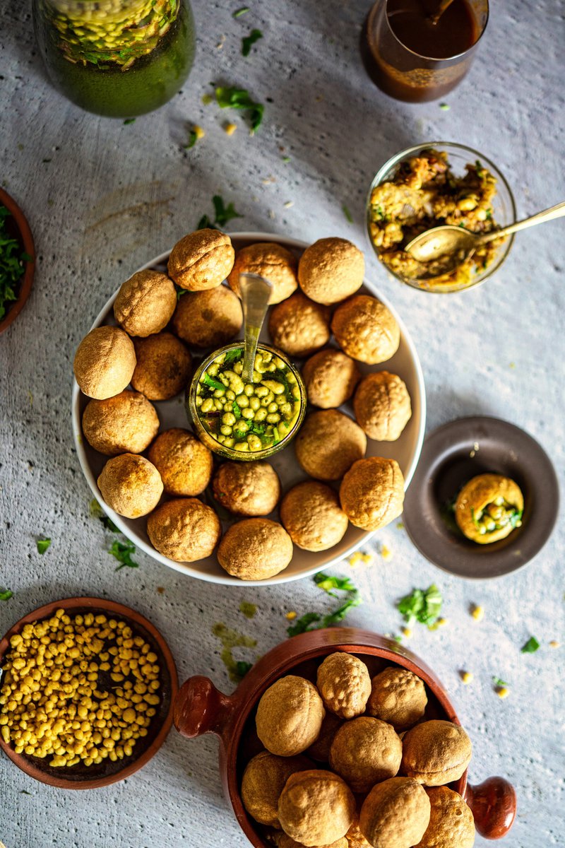 Top view of a spread featuring a plate of puris, a glass of pani, various fillings, and garnishes arranged around.