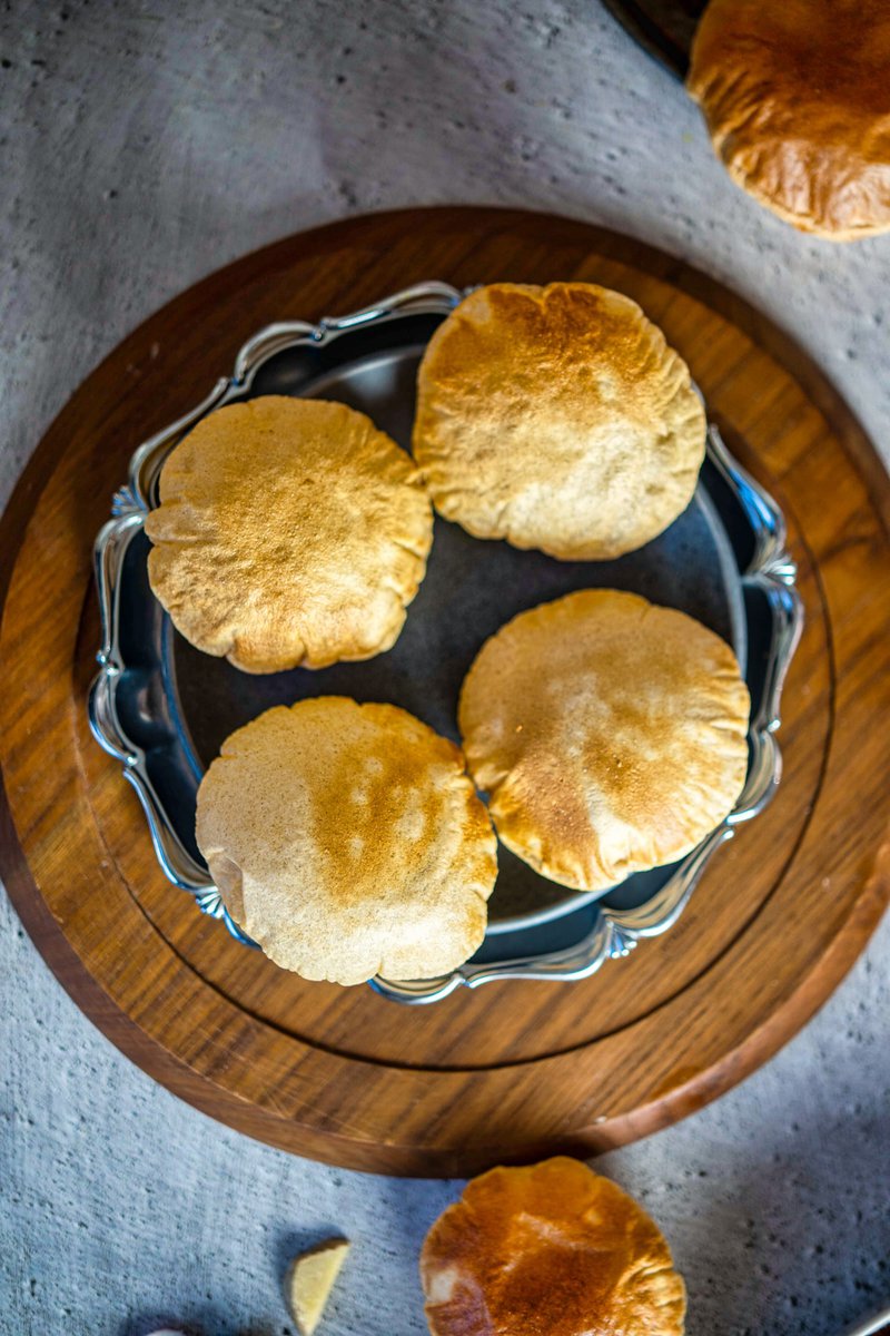 Overhead view of a plate of four air fryer pooris on a wooden tray with a vintage silver rim, set on a concrete surface. The pooris are served with a variety of curries and chutneys.