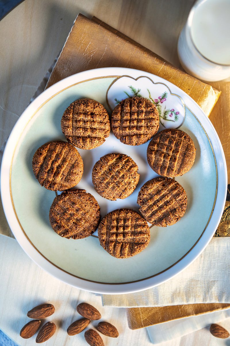 Top view of a plate with round almond date cookies and a glass of milk on the side.