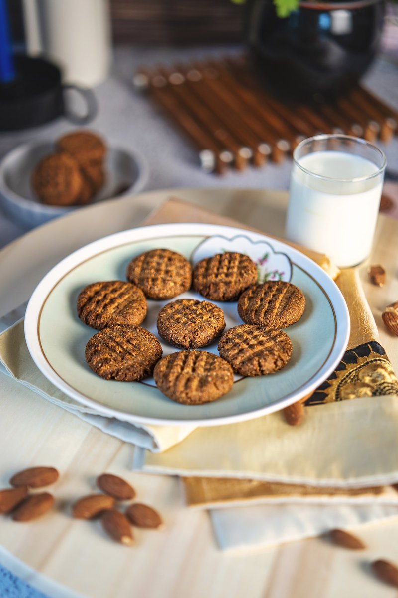 Plate of almond date cookies next to a glass of milk, with scattered almonds in the background.