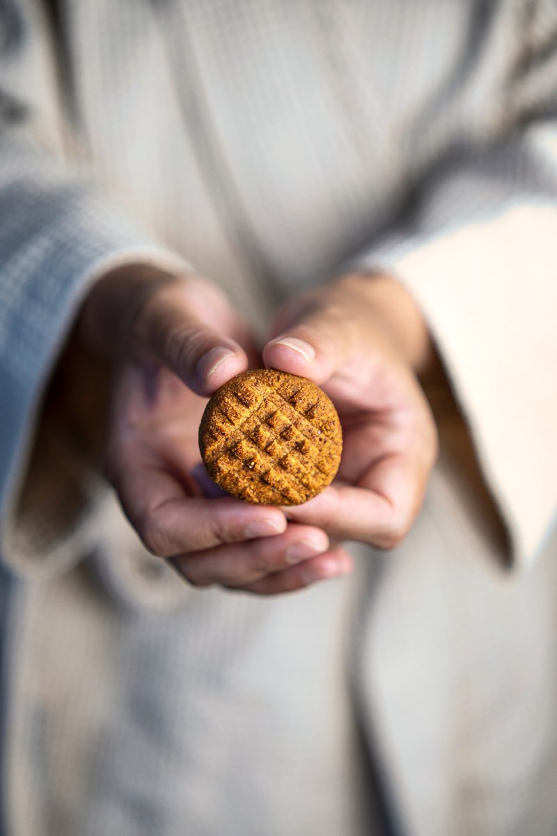 A person holding a round almond date cookie with a crisscross pattern.