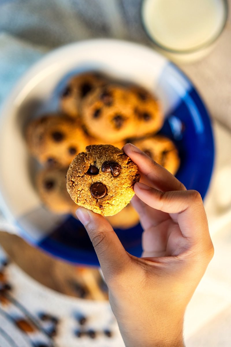 Homemade almond flour chocolate chip cookies in a blue and white bowl, with one cookie held above the bowl.