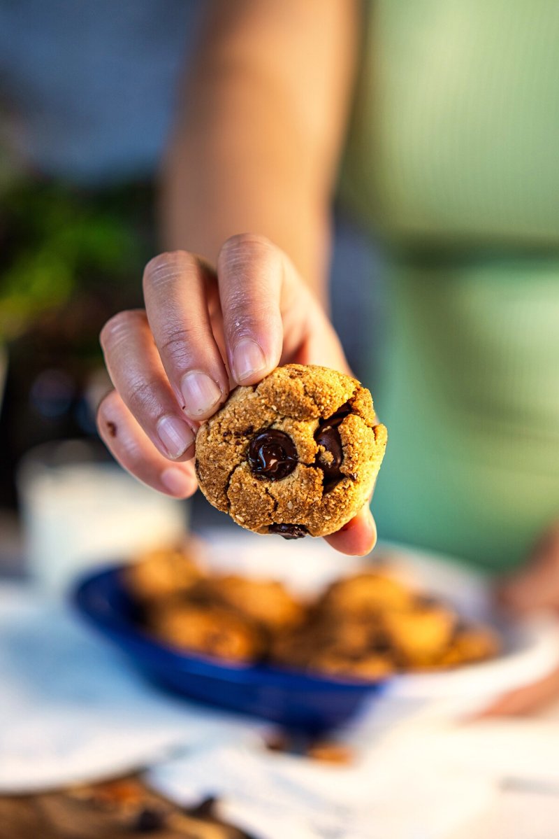 Almond flour tahini chocolate chip cookie held in hand, showing its soft centre and melted dark chocolate chips.