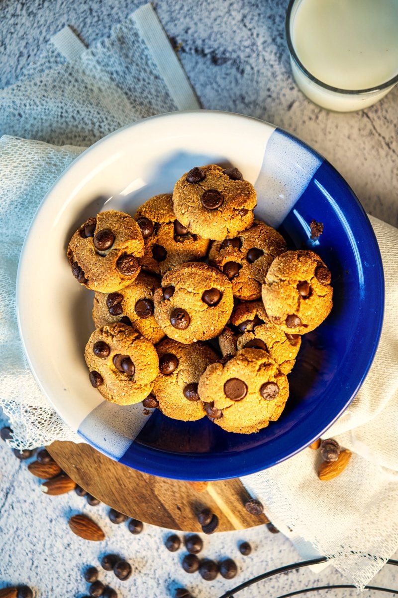 Overhead view of homemade almond flour chocolate chip cookies piled in a blue and white bowl, served with milk.
