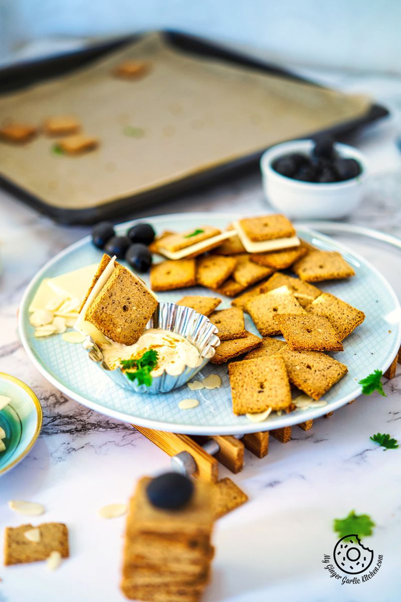 two almond flour crackers  sandwiched with vegan cheese in a dip with more almond crackers on a plate