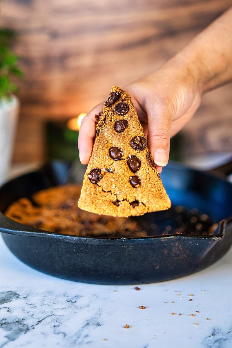 Slice of dairy-free almond flour chocolate chip skillet cookie with dark chocolate chips and flaky sea salt.