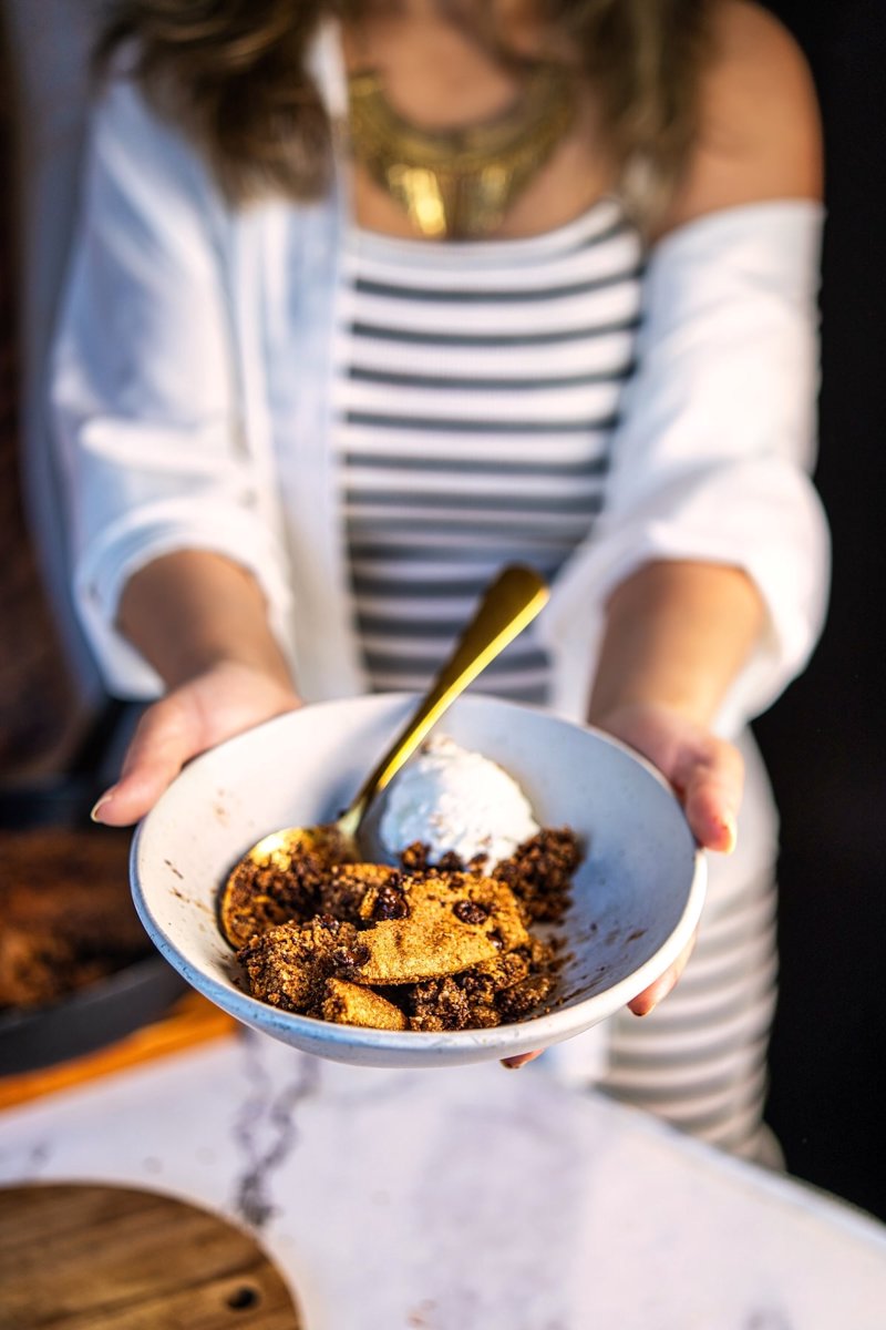 Gluten free warm almond flour chocolate chip skillet cookie served in a bowl with vanilla ice cream and melted dark chocolate.