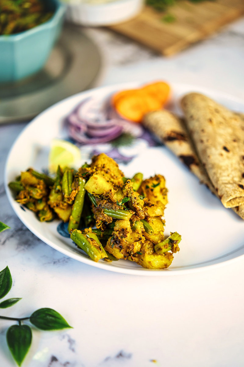 A vibrant bowl of Aloo Beans garnished with fresh cilantro and a lemon wedge.