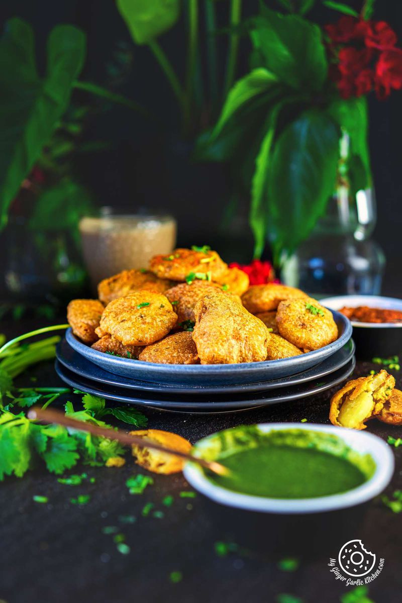 a plate of fried aloo pakora with green chutney and a vase of flowers