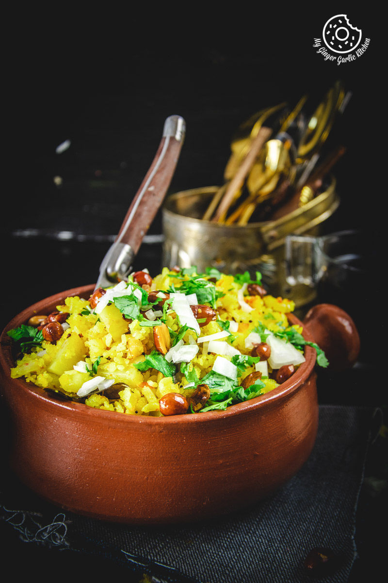 a bowl of aloo poha topped with peanuts, onions and lime wedge on a table