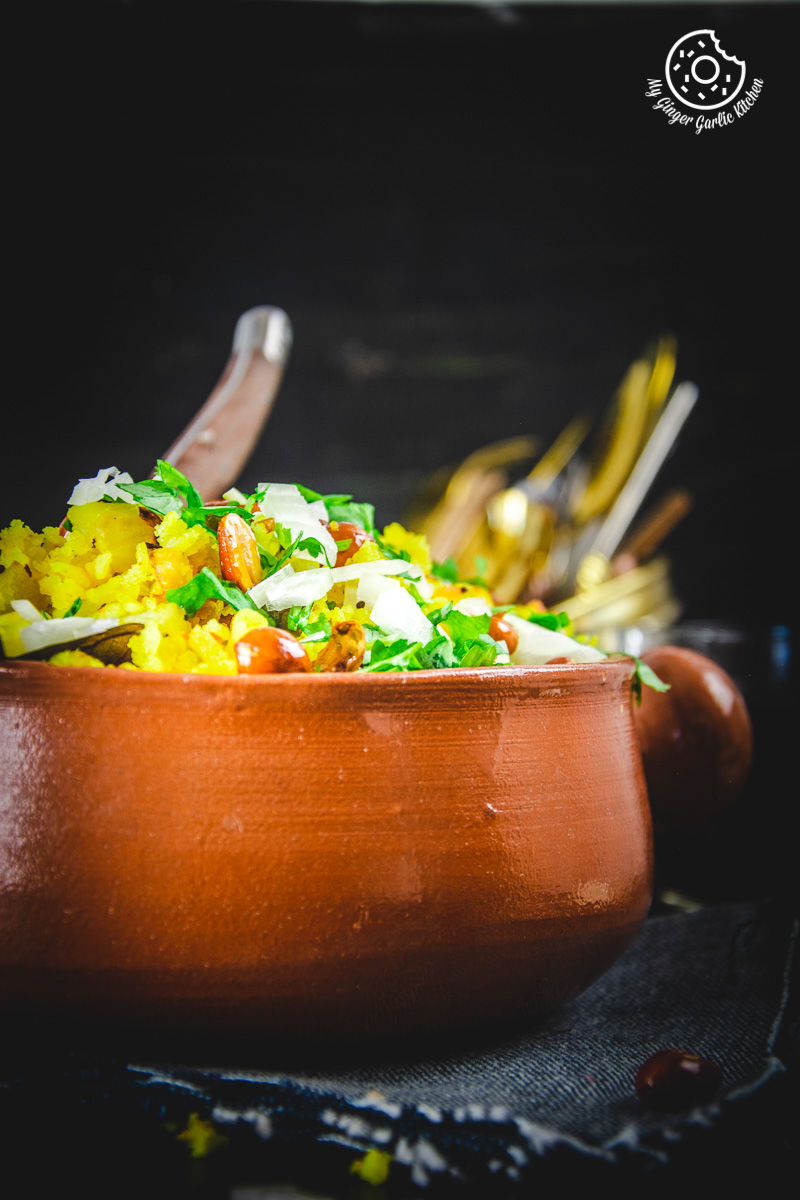 a bowl of aloo poha topped with peanuts, onions and lime wedge on a table