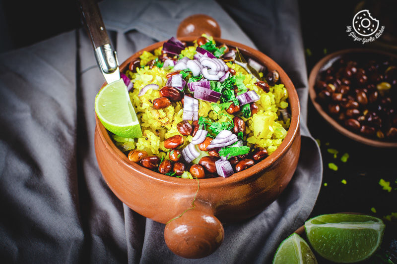 a bowl of aloo poha topped with peanuts, onions and lime wedge