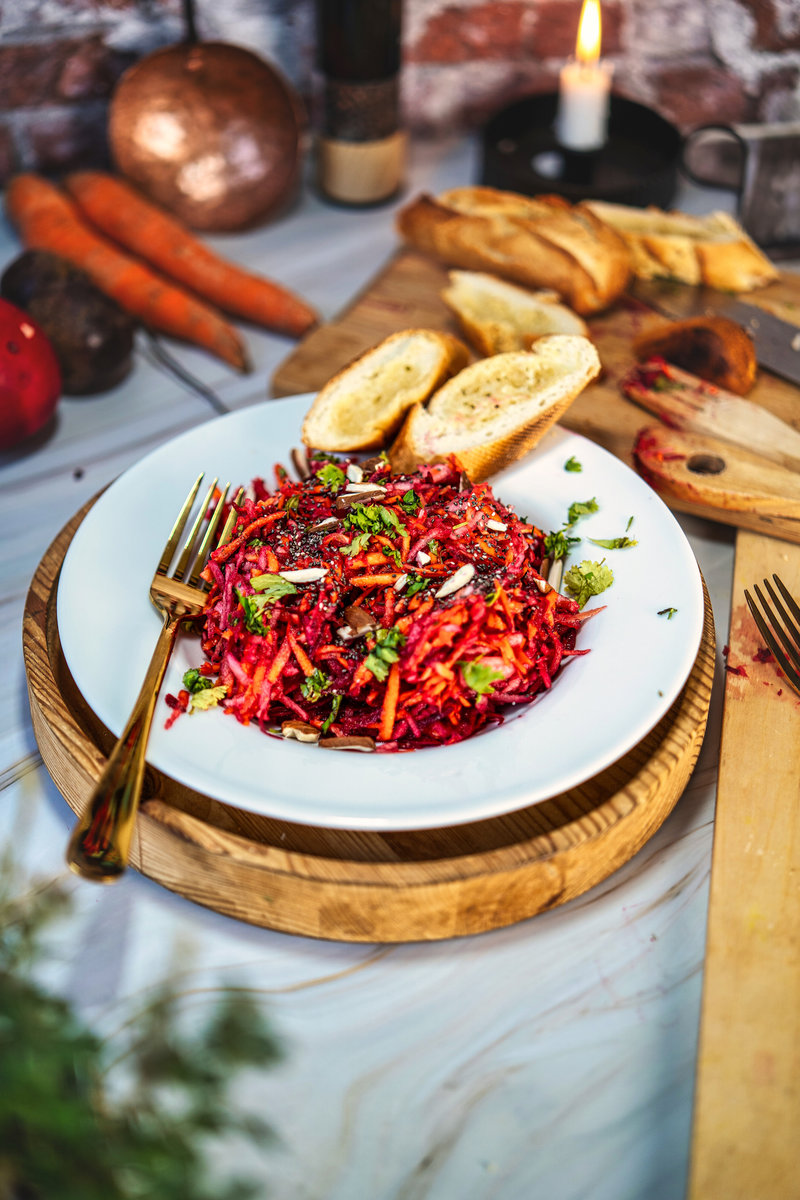 Vibrant apple beetroot carrot salad on a white plate with sliced bread, perfect for a healthy meal.