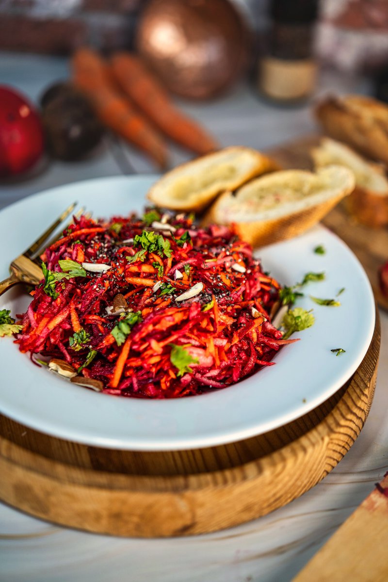 Close-up of a fresh apple beetroot carrot salad garnished with herbs, served with bread on a wooden platter.