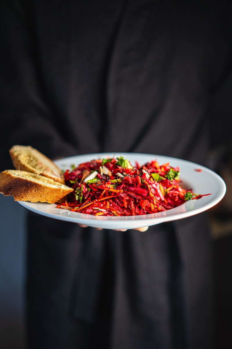 Handheld plate of apple beetroot carrot salad with bread, highlighting vibrant colors and healthy ingredients.