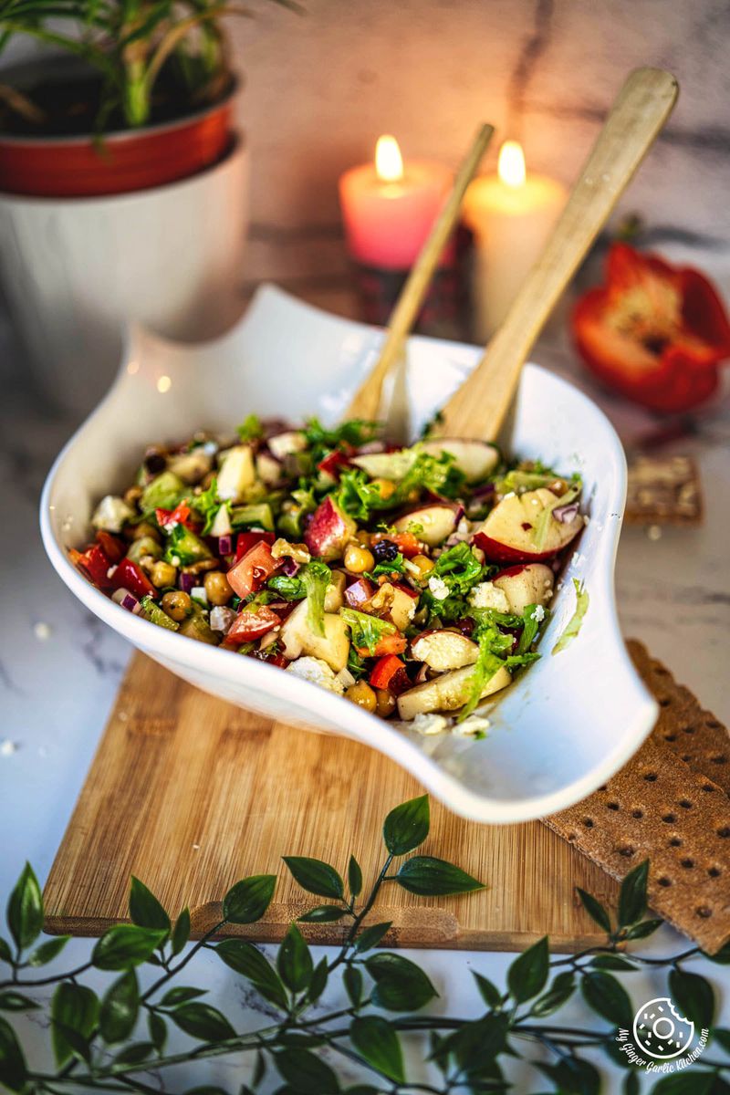 a bowl of salad with apples, cucumber and onions on a cutting board in front of a candle