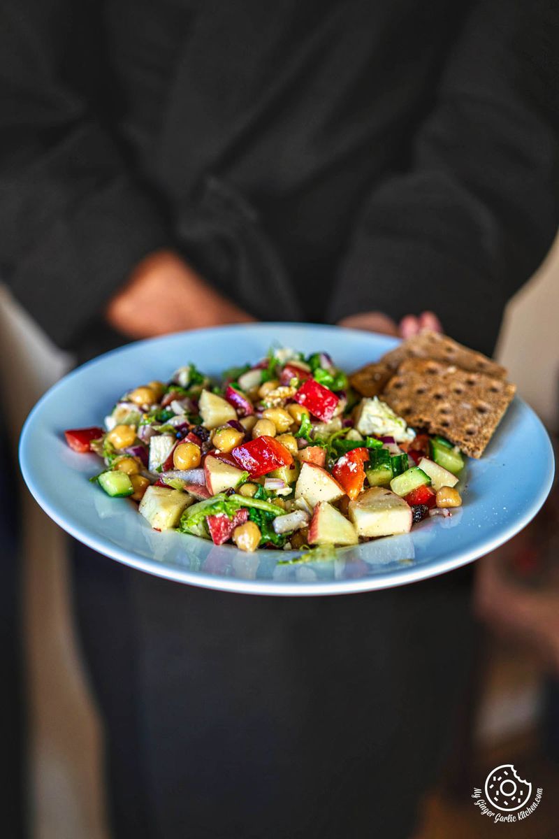 a person holding a whitish blue plate with a apple salad on it