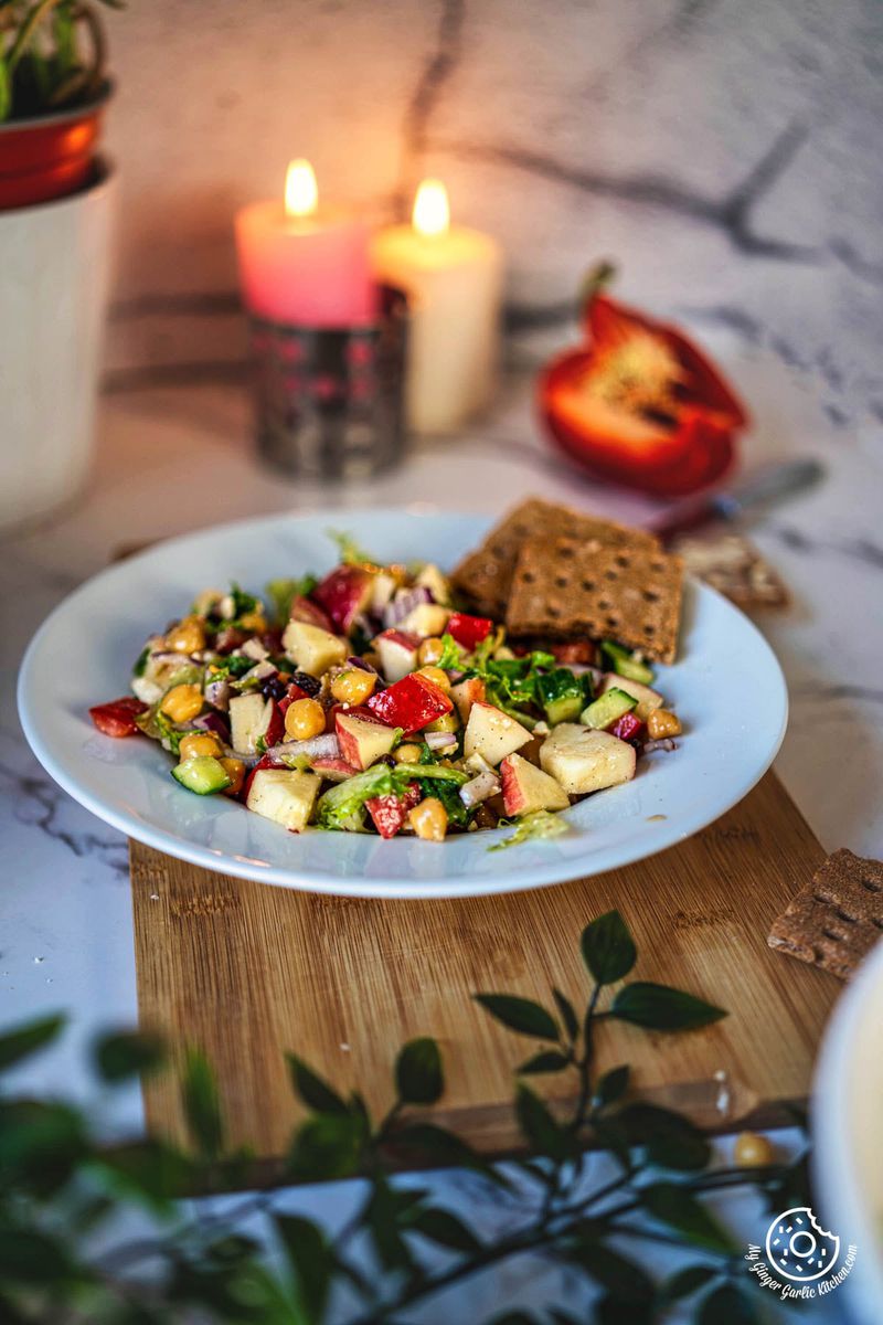 a plate of apple salad on a cutting board with candles in the background