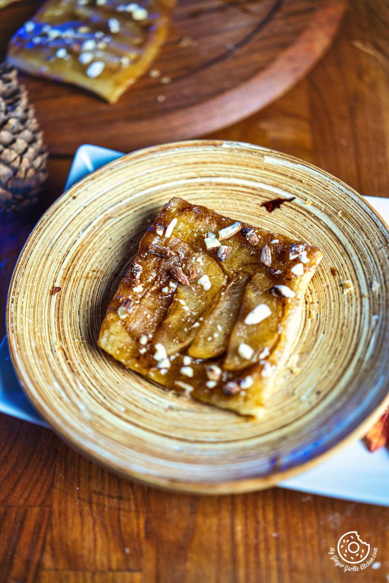 a small piece of apple upside down puff pastry tart on a plate next to a pinecone
