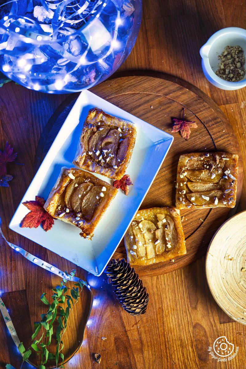 a plate of apple puff pastry tarts on a wooden table with pine cones and blue lights in the background