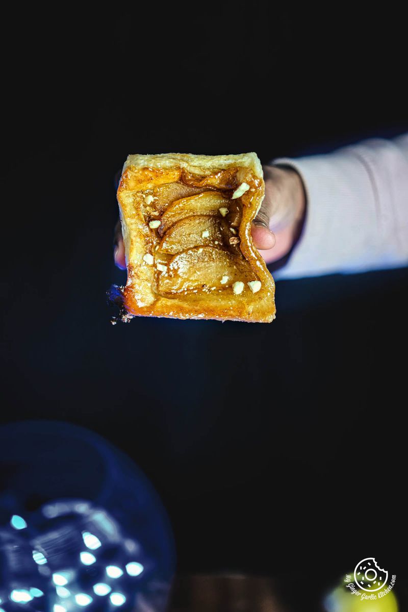 a person is holding up a piece of apple upside down puff pastry with almonds on it