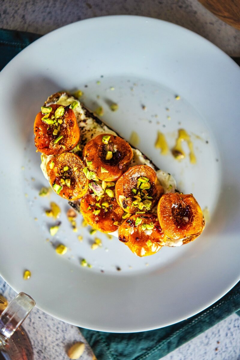 Close up of sourdough toast with grilled apricots, whipped cottage cheese, pistachios, and honey on white plate