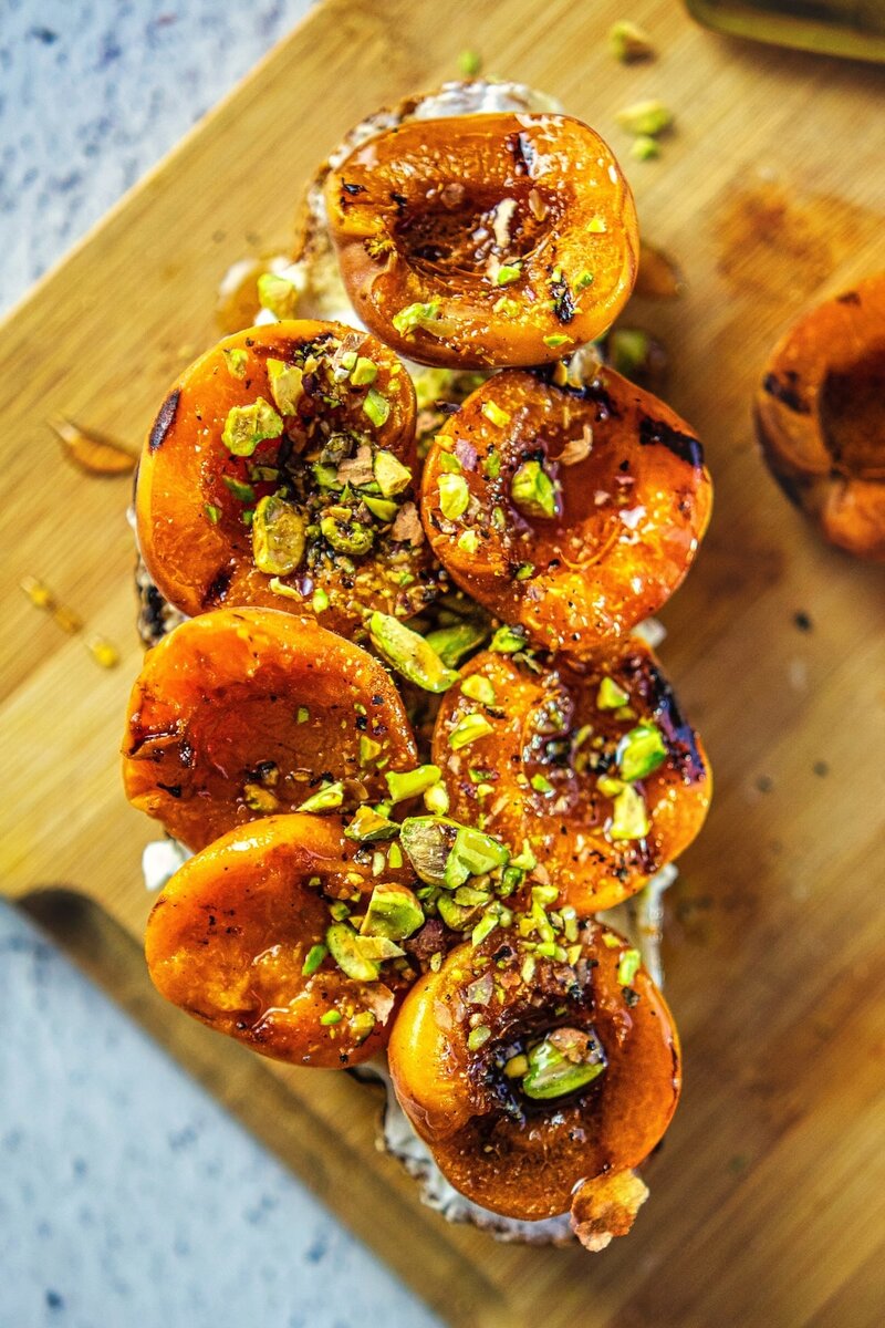 Overhead view of apricot pistachio honey cottage cheese toast on wooden board with caramelized grilled apricots