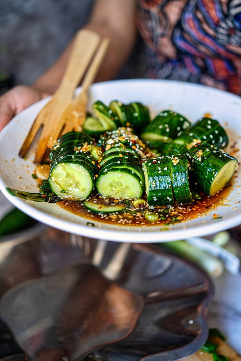 Person holding plate of Asian cucumber salad with wooden utensils